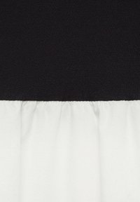 Der obere Abschnitt ist schwarz mit einer glatten Textur, während der untere Teil aus weißem, gerafftem Stoff besteht. Die kontrastierenden Farben schaffen ein zweifarbiges Design.
