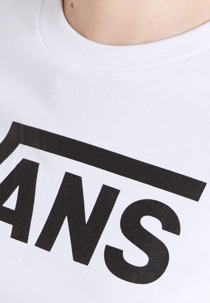 Valkoinen pyöreäkauluksinen paita, jossa on suuret mustat rohkeat kirjaimet "ANS" ja niiden yläpuolella vaakasuora musta viiva, jota käyttää henkilö.