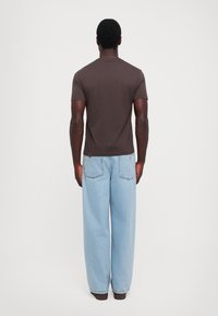 Tricou scurt, maro, cu mânecă scurtă, asortat cu blugi largi, de culoare albastru deschis, având o croială lejeră și un detaliu texturat pe eticheta din spate.
