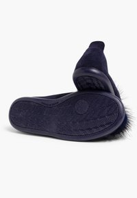 Chaussons en daim bleu marine avec une semelle texturée, ornés d'un accent en fourrure douce au niveau du talon. Design plat avec un bout arrondi.