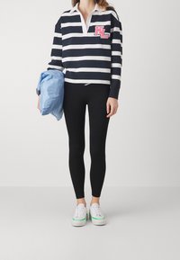 Suéter a rayas en azul marino y blanco con un cuello blanco, que presenta un logo rosa. Combinado con leggings negros y zapatillas blancas con detalles en verde.