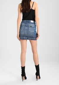 Denimminikjol med fransad nederkant, ljusblå tvätt och två bakfickor. Bärs med en svart linne och svarta klackstövlar.