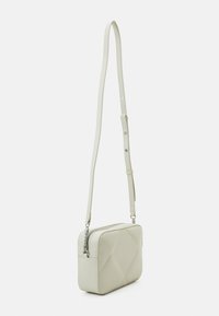 Bolso crossbody color beige claro hecho de cuero suave con un patrón acolchado. Presenta una correa desmontable y herrajes en tono plateado.