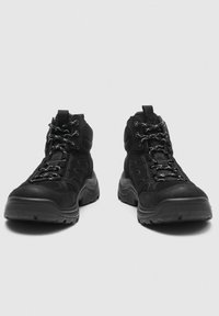 Paire de bottes de randonnée noires avec semelles épaisses et lacets à motifs, vues de face sur un fond uni.