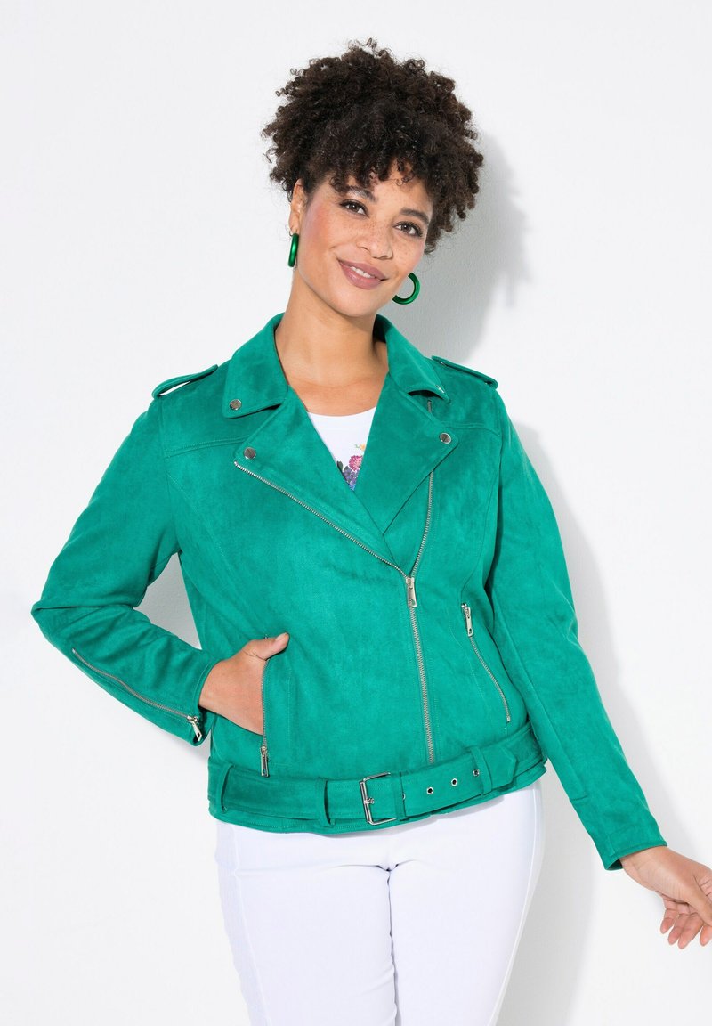 Giubbotto da moto in suede verde con tasche con zip e vita con cintura. Presenta un colletto a risvolto e cuciture alla moda.