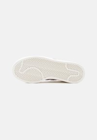 Λευκή σόλα αθλητικού παπουτσιού από καουτσούκ με ζιγκ ζαγκ μοτίβο πρόσφυσης, με λείο, ελαφρώς ανυψωμένο άκρο και χωρίς ορατά λογότυπα ή διακοσμήσεις.