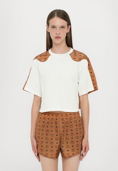 Cropped white top with brown patterned sleeves, featuring a crew neck and logo detail. Paired with brown shorts displaying the same pattern.