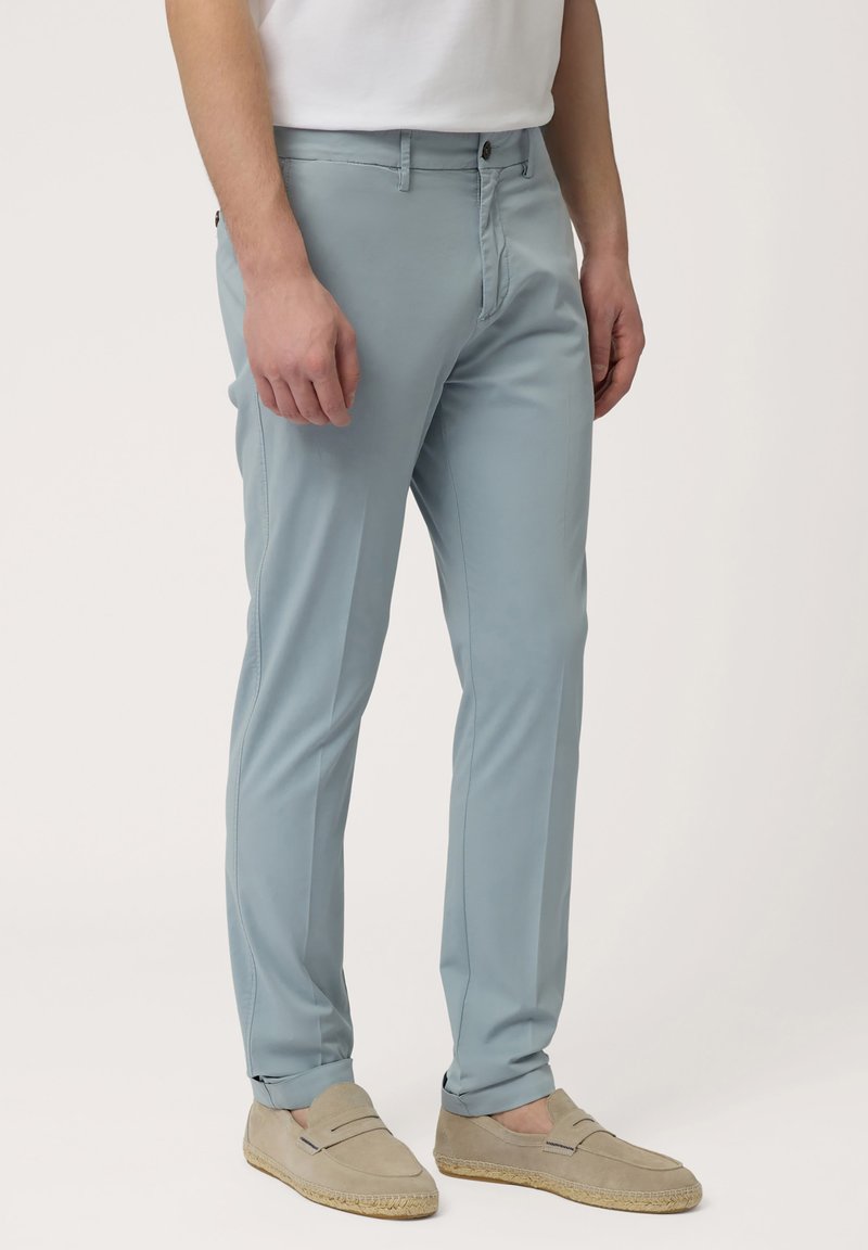 Lichtblauwe broek in een slim fit ontwerp, met een knoopsluiting, zijzakken en een gladde textuur. Gecombineerd met beige instappers.