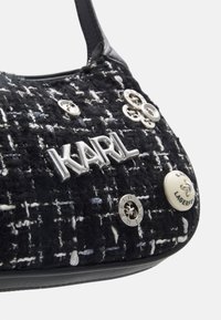 Sac à main en tweed noir et blanc avec quincaillerie argentée, présentant le nom de la marque "KARL" et des boutons décoratifs, bordé de cuir noir.