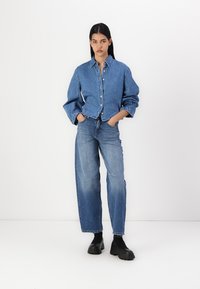 Giacca di jeans con design a bottoni, vestibilità comoda e maniche lunghe, abbinata a jeans blue a vita alta e gamba ampia, insieme a stivali neri chunky.