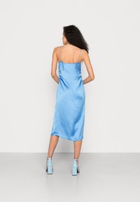 Vestido midi de satin em azul claro com alças finas ajustáveis, franzido lateral e detalhe de fenda. Combinado com sandálias de salto bloco em azul claro.