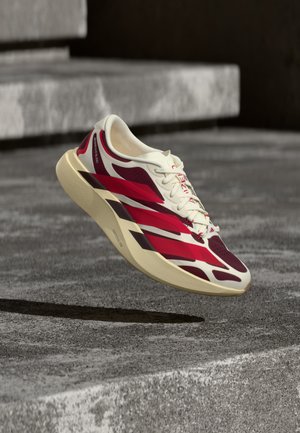 Baskets de sport blanches et rouges avec une semelle épaisse flottant au-dessus de marches en béton gris texturé.