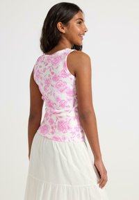 Hvid tanktop med pink blomsterprint, ribbet tekstur og brede stropper, parret med en flydende hvid lagdelt nederdel.