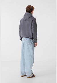 Grå hættetrøje med en afslappet pasform, parret med lyseblå vide jeans. Har ribbede manchetter og to baglommer.