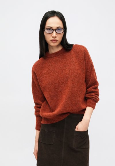 Ruusakaspunase tooniga kudumisseest, millel on ümmargune kaelus ja soonilised varrukaotsad, kombineeritud tumeda seemisnahast seelikuga, millel on kaks esimest taskut.