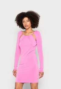 Vestido justo de mangas longas em tecido rosa brilhante. Apresenta decote arredondado com recortes nos ombros. Textura suave e ligeiramente elástica.