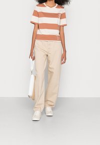 Camiseta de manga corta a rayas en beige y óxido, con texto gráfico. Combinada con pantalones rectos de color beige claro y zapatillas blancas.
