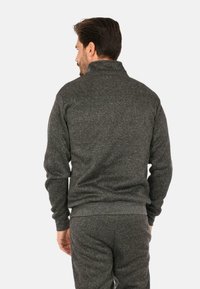 Giacca in pile grigio scuro con colletto alto e polsini a coste. Presenta un tessuto texturizzato e una vestibilità comoda, adatta per un abbigliamento informale.