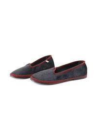 Zapatos de ante negro tipo slip-on con ribete rojo y suela de goma texturizada, presentando una punta redondeada y un diseño minimalista.