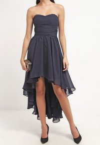 Mörkblå strapless hög-låg klänning i mjukt tyg, med en figursydd överdel och en flödande kjol med lagerkant, ihop med en liten kuvertväska.