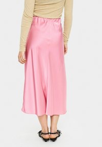 Roze satijnen midi-rok met een elastische tailleband, gladde textuur en een vloeiende silhouet. Gecombineerd met zwarte sandalen met strikken.