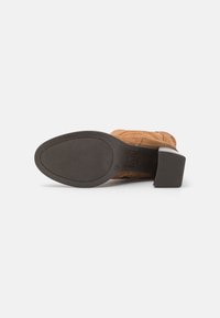 Bottine en daim marron avec un bout carré, semelle en caoutchouc noir épais et talon empilé ; détails de couture visibles sur le dessus.