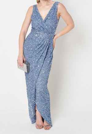 Niebieska wieczorowa sukienka bez rękawów z cekinami, dekoltem w serek, detalem kopertowym i rozcięciem z przodu, noszona z srebrnymi sandałkami z odkrytymi palcami i małą błyszczącą kopertówką.