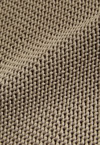 Tissu beige texturé avec un motif tissé dense, affichant une apparence douce et surélevée ainsi qu'une distribution uniforme des points sur la surface.