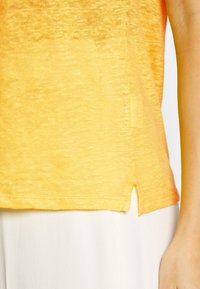 Žlutá košile s krátkým rukávem, vyrobená z texturované látky, s mírně zakřiveným lemováním a postranními rozparky pro větší pohyblivost.