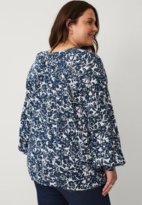 Marineblauwe en witte bloemenblouse met lange mouwen, geplooide halslijn en gestructureerde stof. Versterkt met een ontspannen pasvorm en vloeiende ontwerpen.