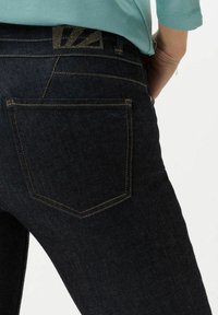 Vaqueros de mezclilla oscura con un ajuste slim, que presentan costuras doradas en contraste, bolsillos estándar y un detalle texturizado en la cintura.