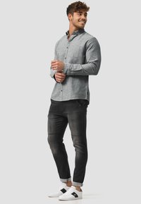 Gray button-up shirt with collar, long sleeves, and a pocket, paired with dark jeans and white sneakers featuring black accents.