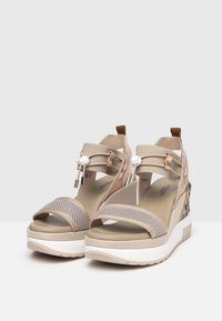 Beige platformové sandály s textilním svrškem, nastavitelnými popruhy a texturovaným podpatkem s jemným zvířecím vzorem. Bílá gumová podešev.