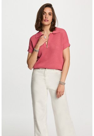 Roze gebreide poloshirt met korte mouwen, ritskraag en gestructureerd patroon, gecombineerd met witte wijde broek en zilveren sieradenaccenten.