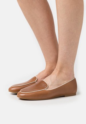 Mocasines de cuero marrón con ribetes blancos, puntas redondeadas y suelas planas, que presentan un sutil logo en la parte superior.