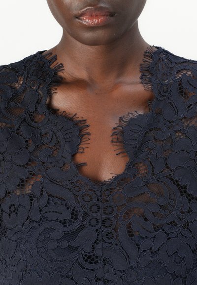 Navy lace dress with floral patterns, scalloped neckline, and frayed edges. Intricate texture and semi-sheer design.