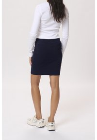 Falda ajustada azul marino con textura suave y cinturilla elástica, combinada con camiseta blanca de manga larga y zapatillas blancas gruesas.