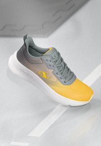 Grau und gelbe Sportschuh mit einem Farbverlauf-Design, strukturierter Oberseite, Schnürung und einer weißen Gummisohle. Enthält ein Logo an der Seite.
