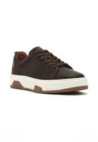 Zapatillas de cuero texturizado marrón con una entresuela blanca y suela de goma beige, que presentan un diseño de cordones y un detalle de costura.
