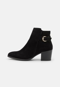 Stivale alla caviglia in suede nero con punta arrotondata, gambale corto e tacco a blocco. Presenta una cinturino decorativo con fibbia sul lato.