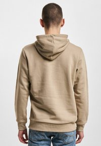 Beige Kapuzenpullover mit Kordelzug, gerippten Bündchen und Saum. Der Stoff wirkt weich und hat eine glatte Textur mit einer lockeren Passform.