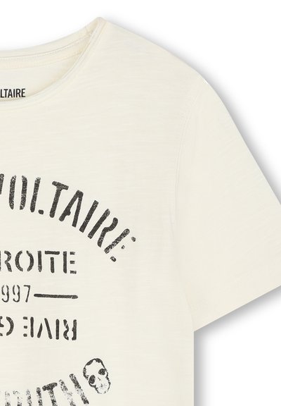 Kremowa koszulka z miękkiego materiału z czarnym nadrukiem z nazwą "Voltaire" i grafiką czaszki. Klasyczny okrągły dekolt i krótki rękaw.