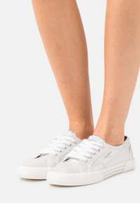 Baskets en toile blanche avec une finition texturée, un design à lacets et un marquage subtil. Présentent une semelle en caoutchouc blanche et des accents argentés.