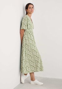 Vihreä kukallinen pitkä mekko lyhyillä hihoilla ja vyötäröltä kiristetty, yhdistettynä valkoisiin tennareihin. Mekossa on valkoisia ja vaaleanvihreitä lehtikuvioita.