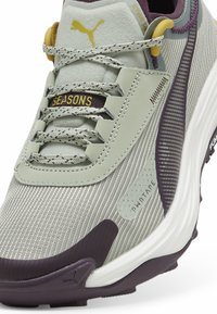 Light green athletic shoe with a textured upper, purple accents, and yellow hardware. Features a sleek design and padded collar for comfort.
