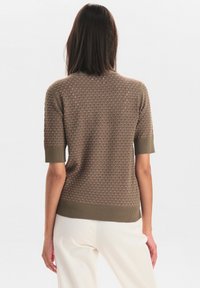 Kortärmad, olivgrön stickad tröja med texturerat mönster och ribbade detaljer vid fållen och ärmarna. Minimalistisk design med bakifrån.