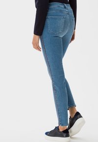 Slim džíny v světle modrém denimu s vysokým pasem, jemným bočním pruhovým detailem a klasickým pětipocketovým designem, doplněné černými teniskami.