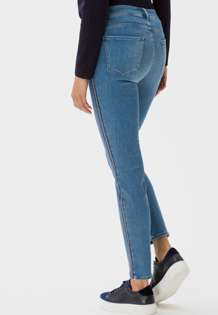 Slim džíny v světle modrém denimu s vysokým pasem, jemným bočním pruhovým detailem a klasickým pětipocketovým designem, doplněné černými teniskami.