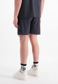 Donkergrijze shorts met een gestructureerd ruitpatroon, gecombineerd met witte sneakers en sokken met zwarte accenten. Slim fit en boven de knie lengte.