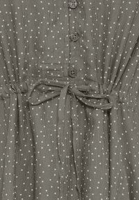 Robe en tissu gris à pois, dotée d'une patte de boutonnage et d'une ceinture nouée à la taille.